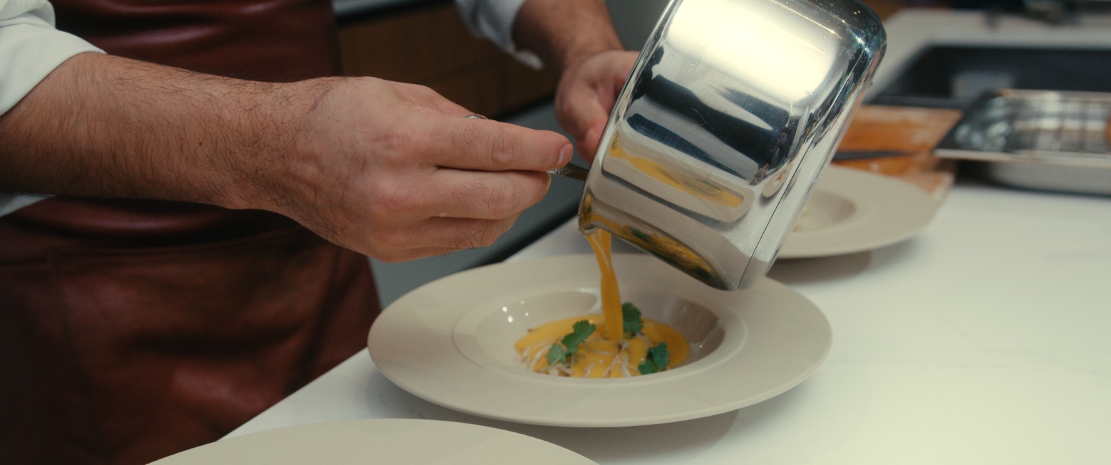 Le chef verse un velouté de potimarron dans une assiette