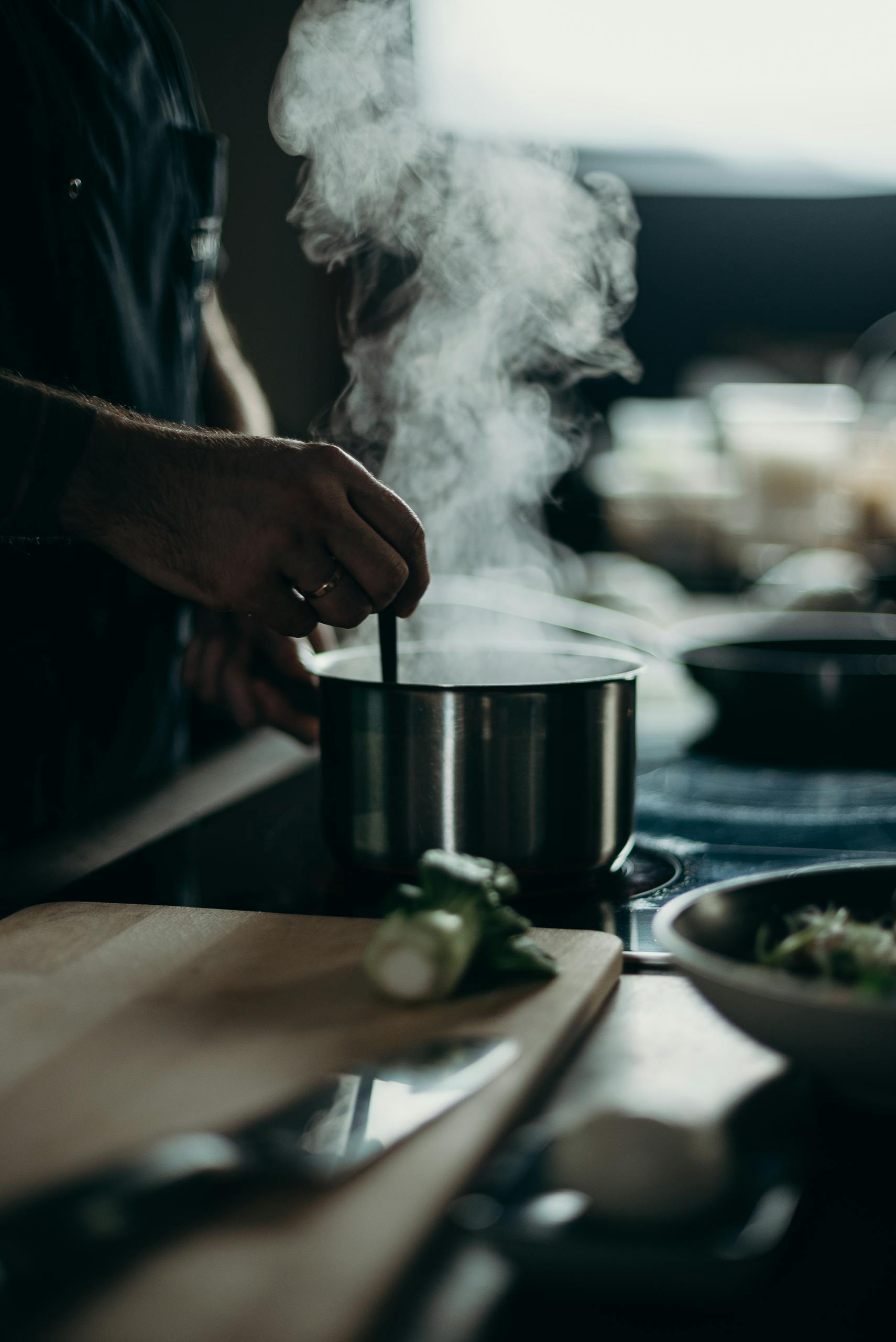 Une personne remuant une casserole fumante sur une cuisinière électrique avec des ustensiles de cuisine étalés.