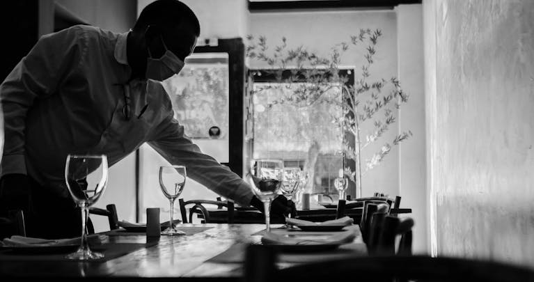 Photo en noir et blanc d'un maître d'hôtel masqué mettant une table dans un appartement du 7 eme arrondissement à Paris.