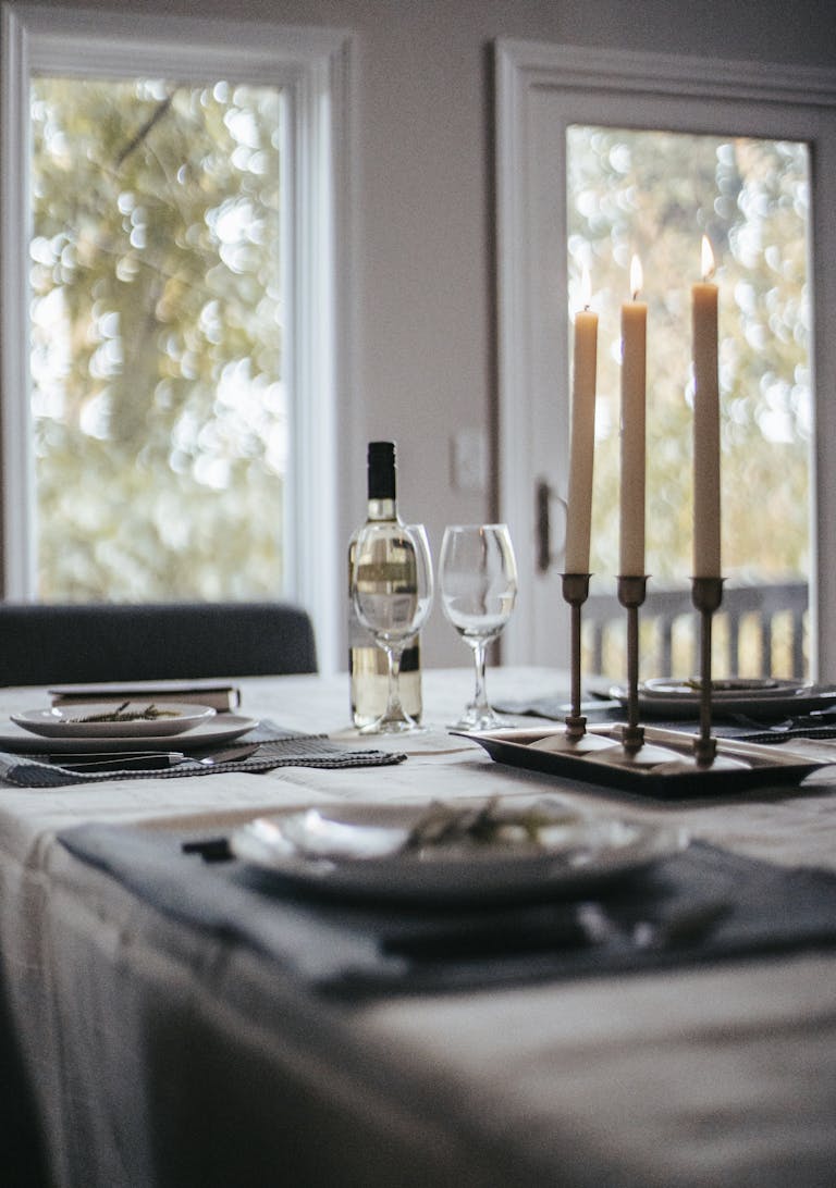 Table dressée avec divers couverts, une bouteille de vin, des verres et des bougies disposés sur une nappe, préparée pour un événement