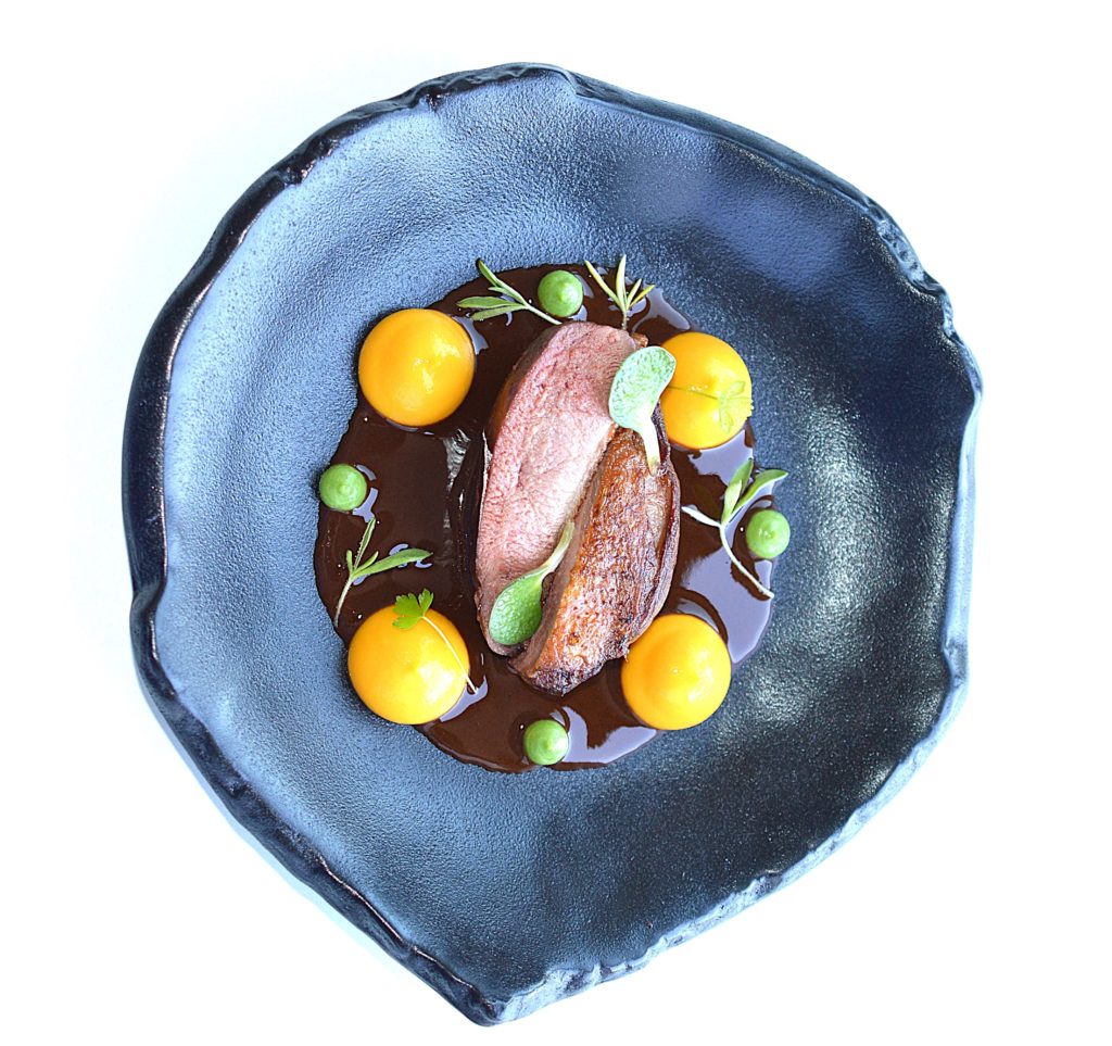 Une assiette noire sublimé par un dressage d'un pigeon et un d'un jus de viande au vin rouge
