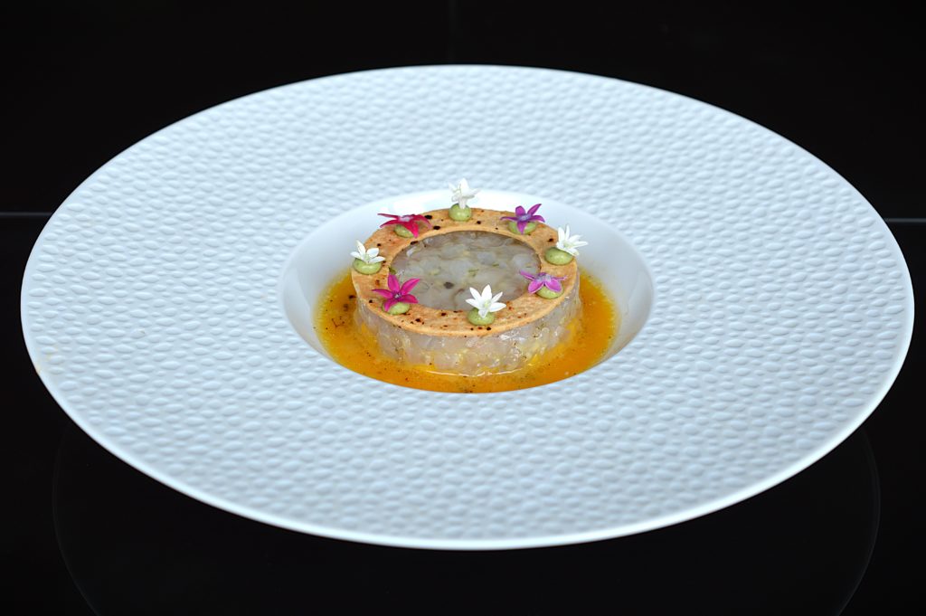 Sea bass tartare plated in a shallow white dish with citrus sauce and edible flowers