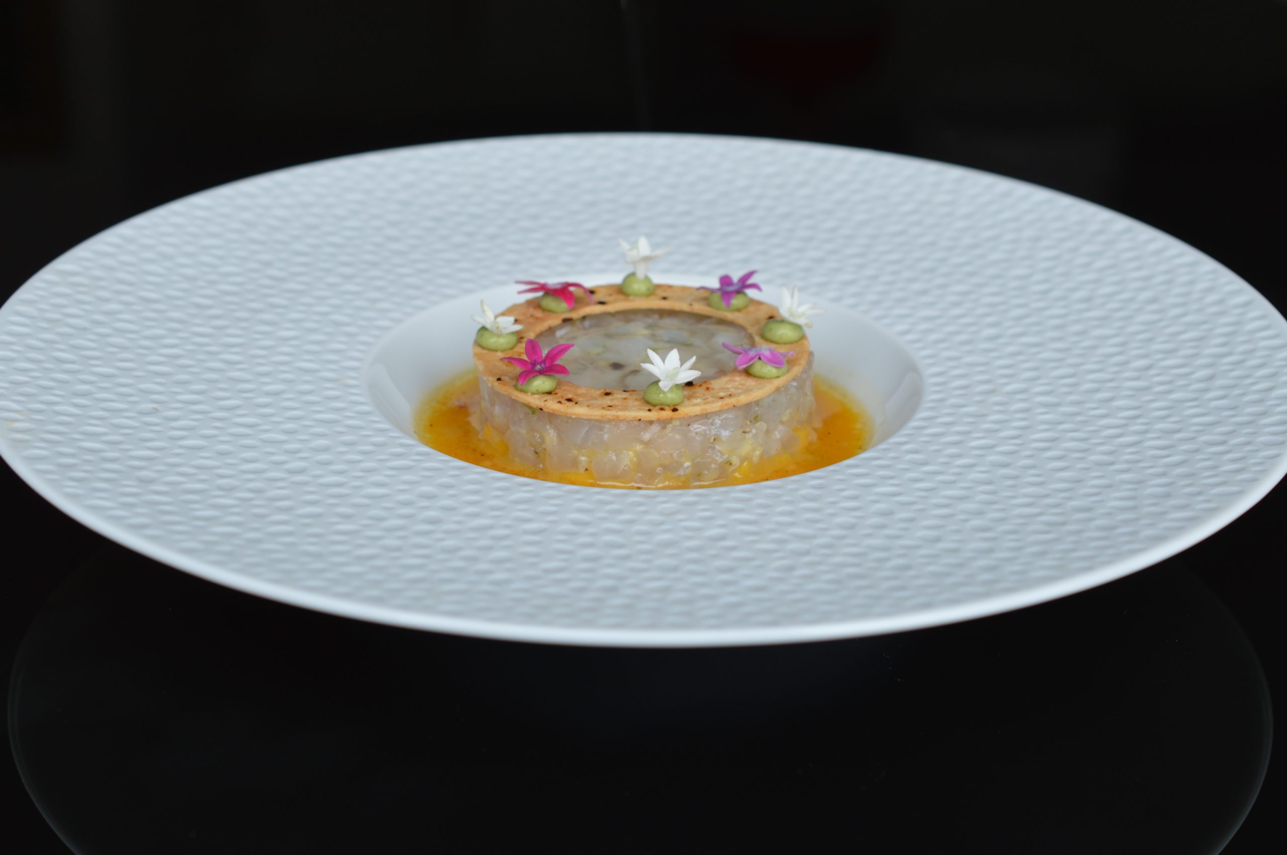 Tartare de bar sur une assiette creuse et un fond noir