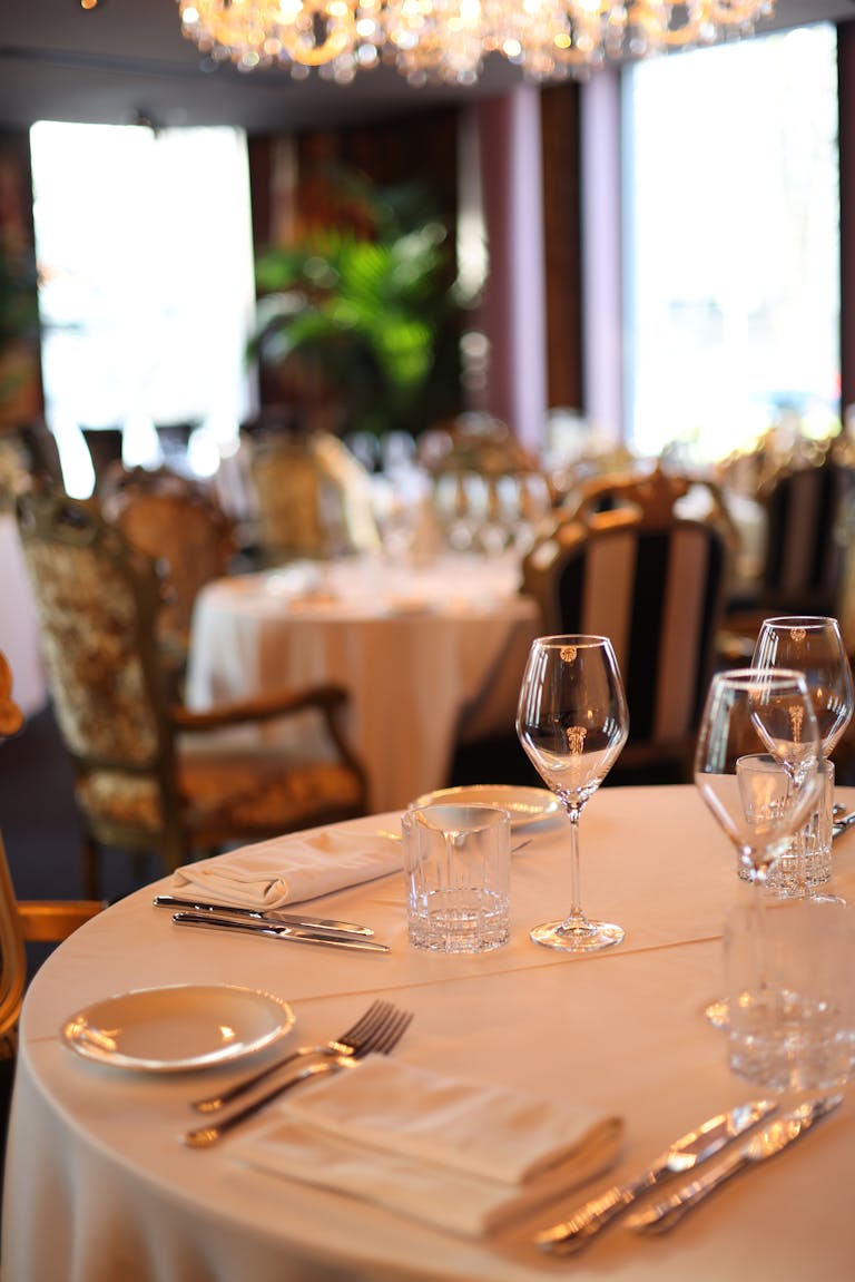 Dressage raffiné d'une table avec verrerie, couverts et une mise au point douce sur l'intérieur luxueux d'un restaurant.