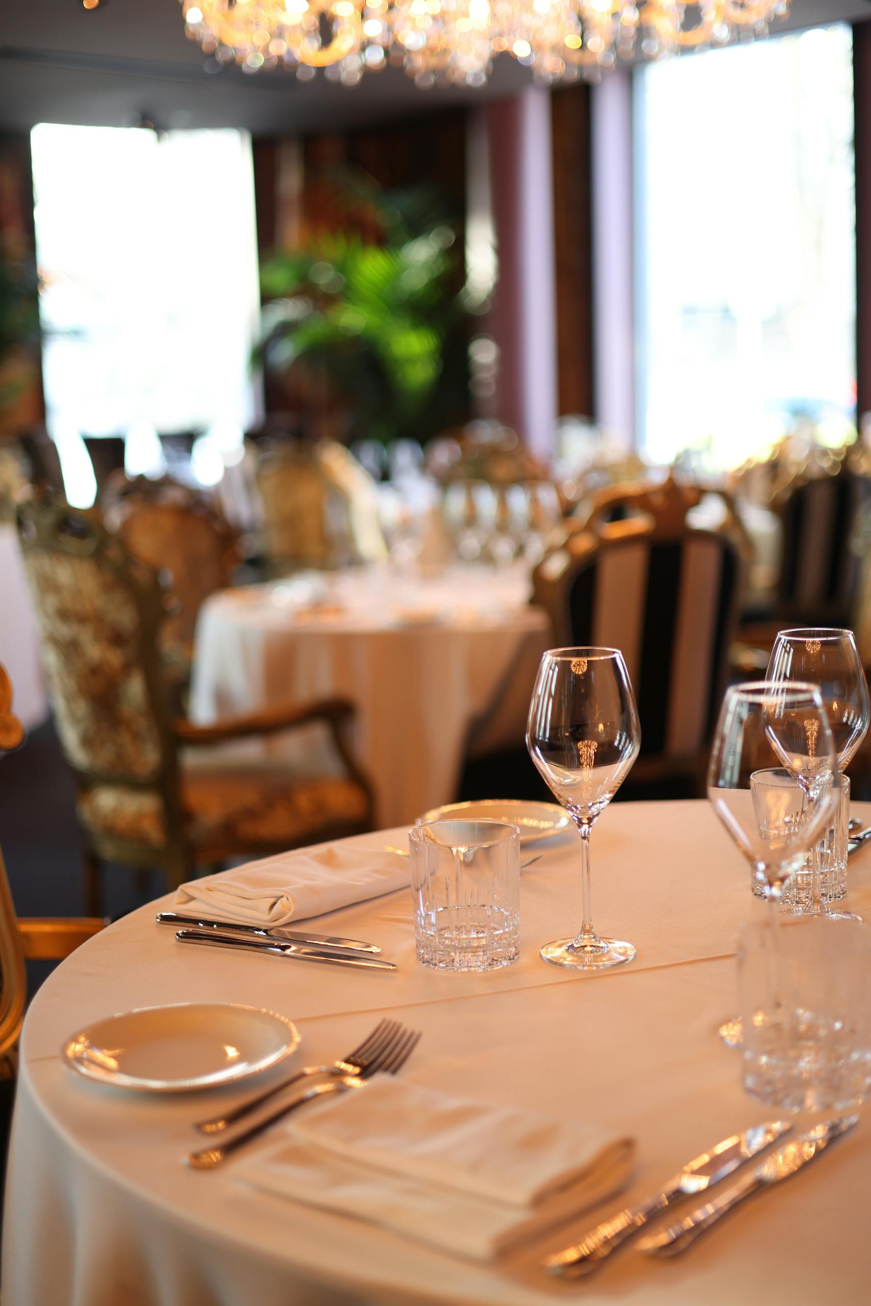 Dressage raffiné d'une table avec verrerie, couverts et une mise au point douce sur l'intérieur luxueux d'un restaurant.