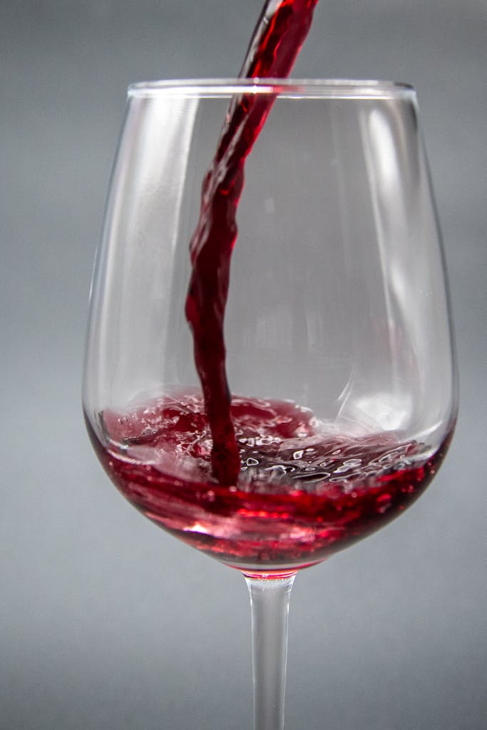 Plan saisissant de vin rouge versé dans un verre transparent sur fond neutre.
