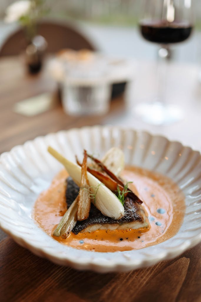 Plat de poisson gastronomique avec une sauce savoureuse, garni de légumes et présenté dans une assiette élégante.