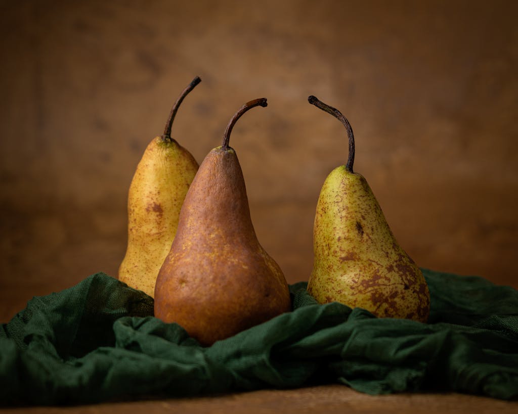 Trois poires fraîches sur un fond de tissu brun rustique, composition classique de nature morte.