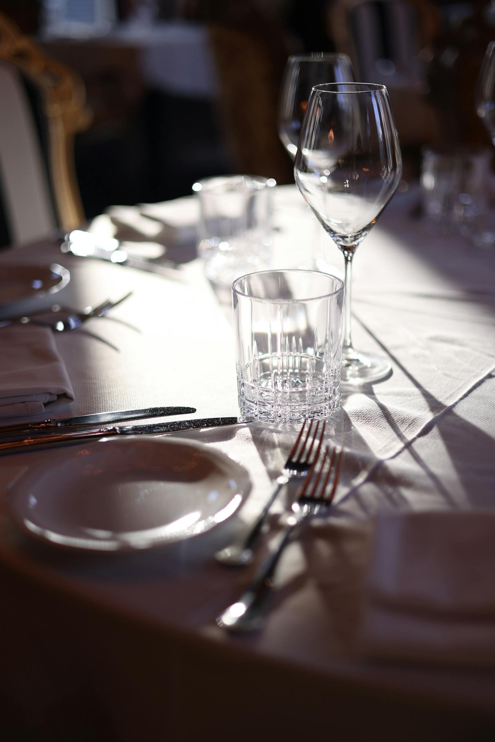 Un cadre raffiné pour une salle à manger élégante, avec couverts, verres et lumière naturelle, pour une expérience culinaire luxueuse.