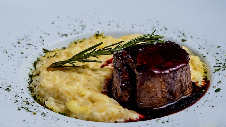 Un délicieux steak d'agneau accompagné d'un risotto crémeux et garni de romarin, parfait pour un repas gastronomique.