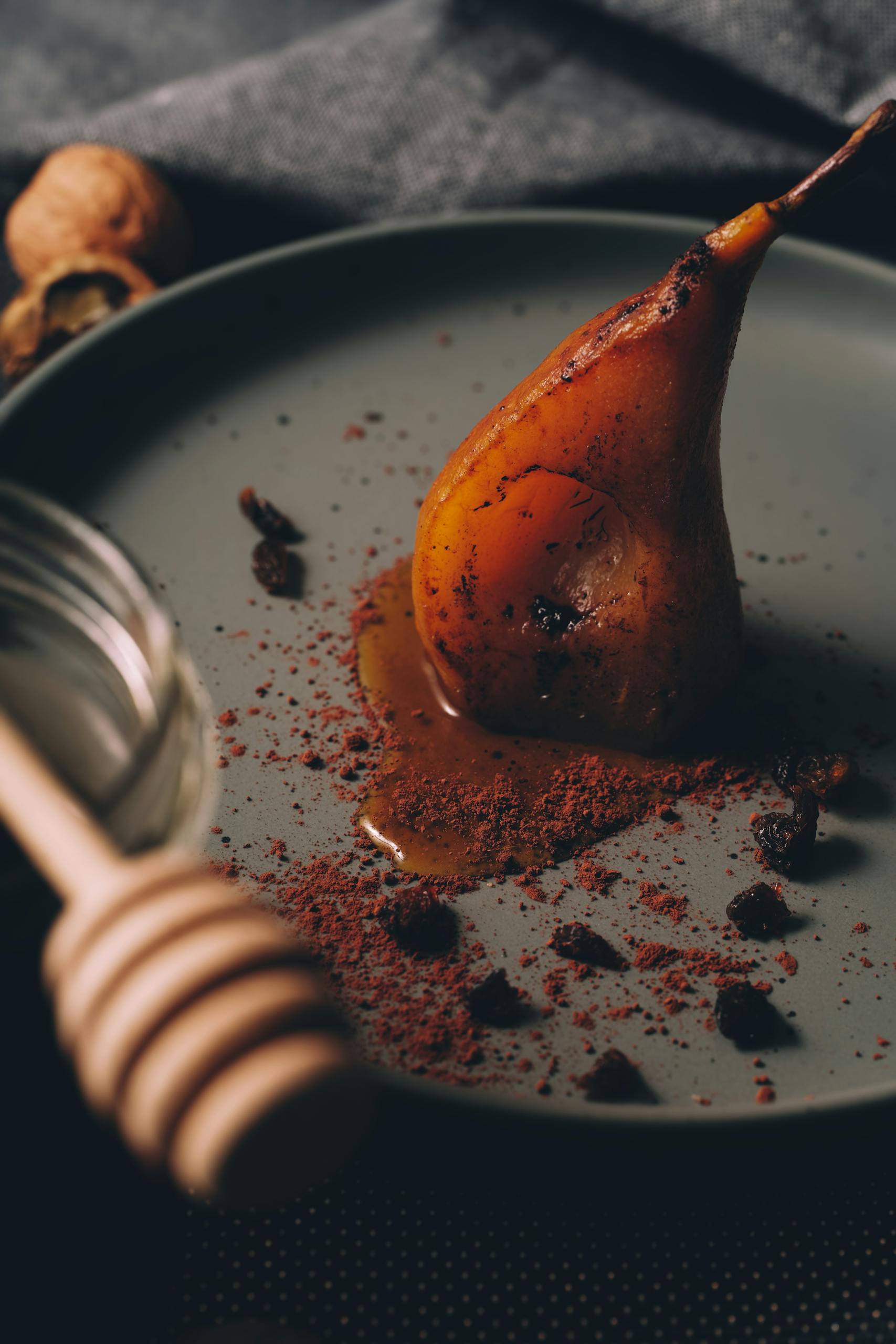 Un dessert de poire pochée magnifiquement présenté sur une assiette, garni de miel et d'épices, créant une ambiance culinaire mystérieuse.