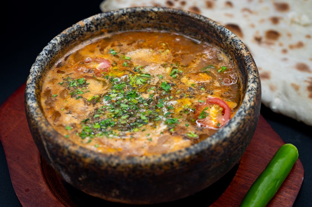 Un ragoût du Moyen-Orient aux saveurs vibrantes, servi dans un bol rustique en pierre avec du pain naan et du piment vert.