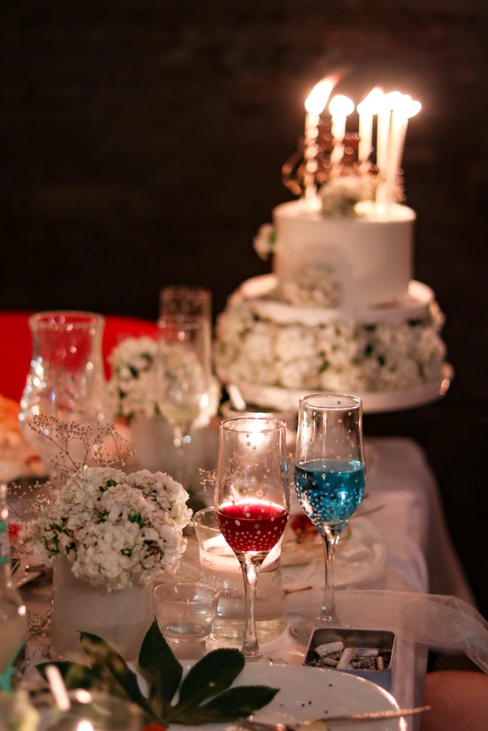 Une table de mariage éclairée aux chandelles, avec gâteau, fleurs et verres à vin. Une ambiance romantique et élégante.