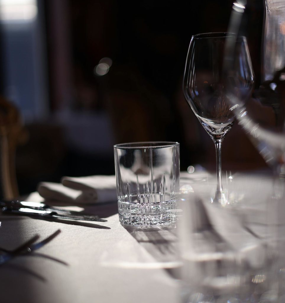 Une table dressée avec élégance, avec des verres et des couverts baignés de soleil sur une nappe blanche.