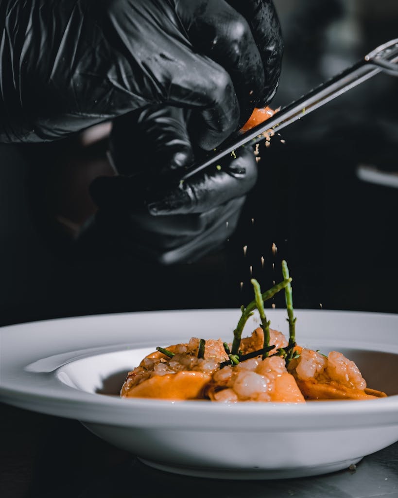 Gros plan sur les mains gantées d'un chef assaisonnant un plat de fruits de mer gastronomique dans la cuisine d'un restaurant.