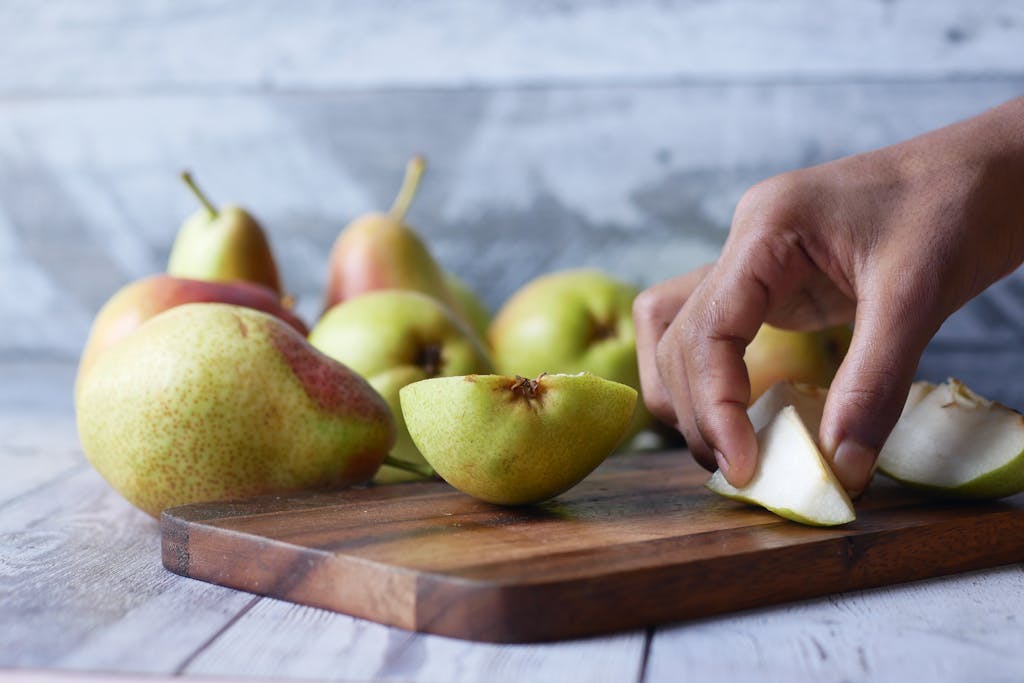 Gros plan sur une main du chef coupant des poires fraîches sur une planche à découper en bois. Idéal pour illustrer le thème de dessert gastronomique française.