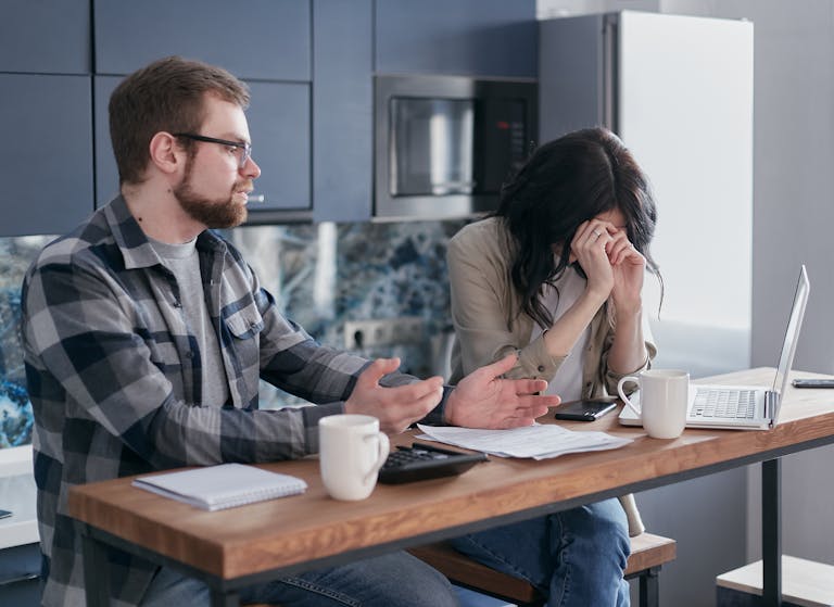 Un couple assis à une table, l'air stressé, discute de problèmes pour organiser un dîner privé à leur domicile